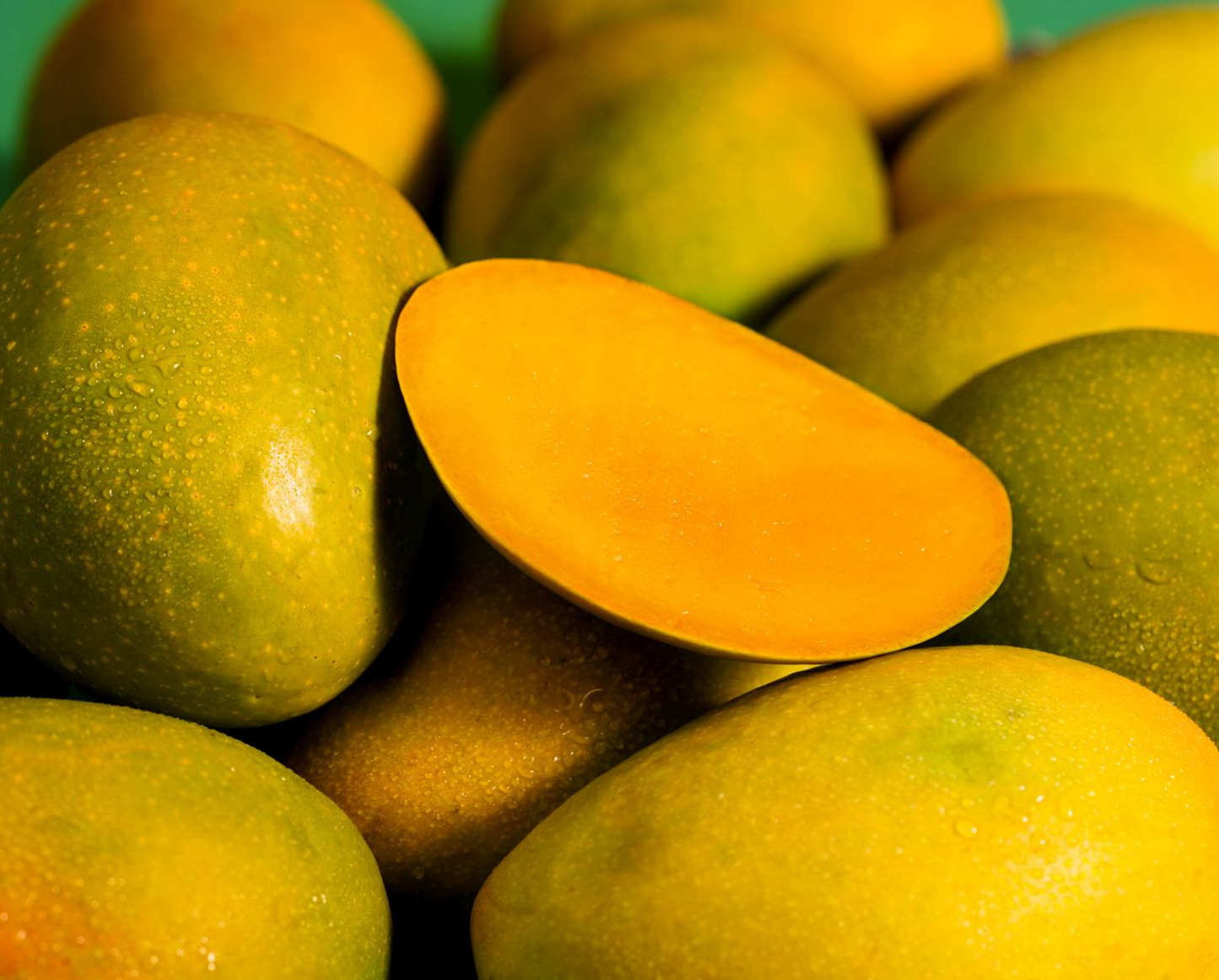 Close-up of green and yellow mangoes with a sliced mango showing its juicy interior. buy alphonso mangoes online India