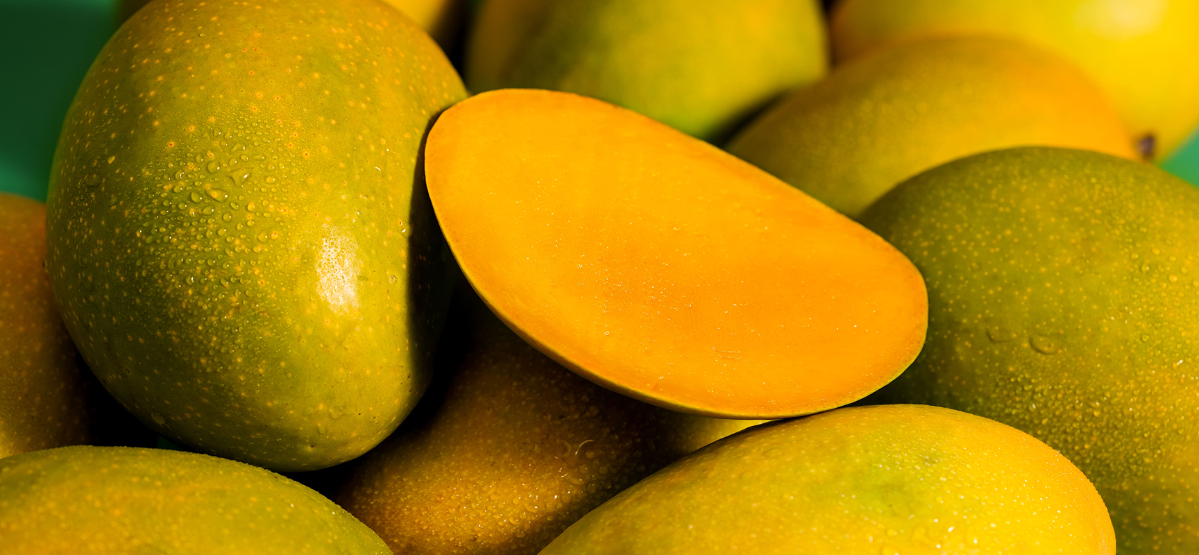 Close-up of green and yellow mangoes with a sliced mango showing its juicy interior.