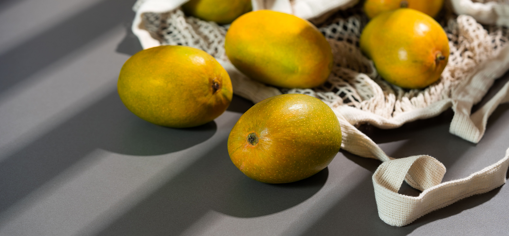 Mangoes on a textured surface with a natural fiber bag. hapus mango online